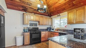 A kitchen with wooden cabinets, a black stove, a granite countertop, and a window.
