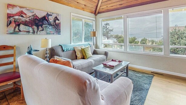 A living room with a wooden ceiling, a painting of horses, a sofa, a chair, and a coffee table.
