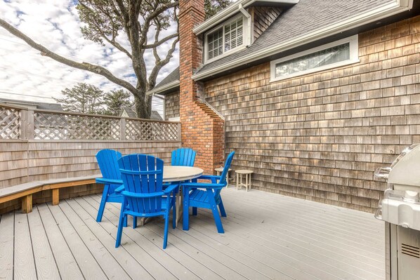 A deck with blue chairs and a table, a brick chimney, and a wooden fence. - Charming cottage 1 block from the Prom & beach with private deck & Ping-Pong (Seaside)