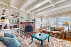 A living room with a fireplace, bookshelves, a sofa, and a coffee table. - Charming cottage 1 block from the Prom & beach with private deck & Ping-Pong (Seaside)
