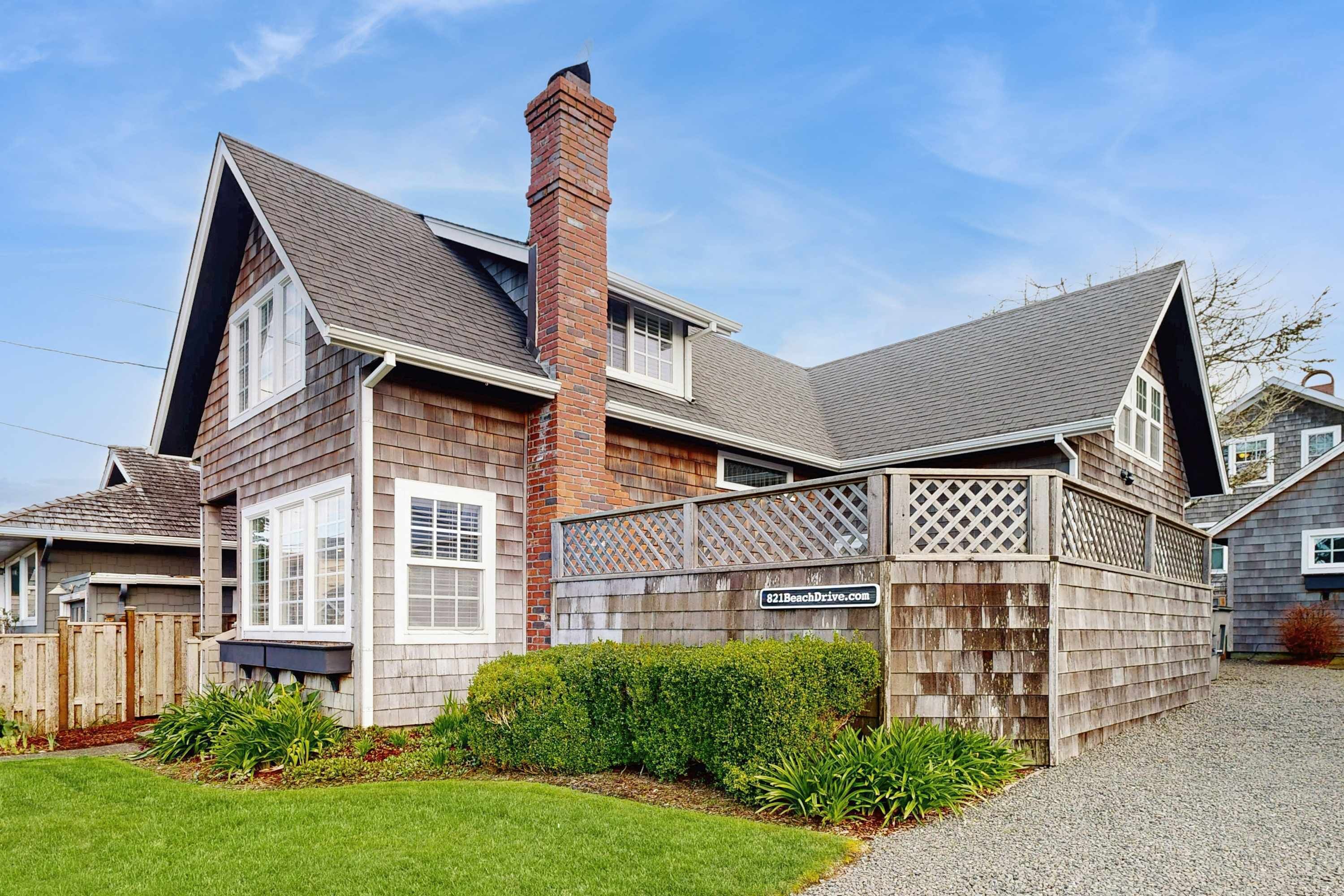 A two-story house with a brick chimney, a wooden deck, and a gravel driveway.