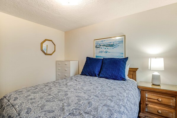 A bedroom with a bed, a dresser, a nightstand, a lamp, and a framed picture on the wall. - Ocean view home with WiFi, gas fireplaces, private washer&dryer, and foosball (Seaside)