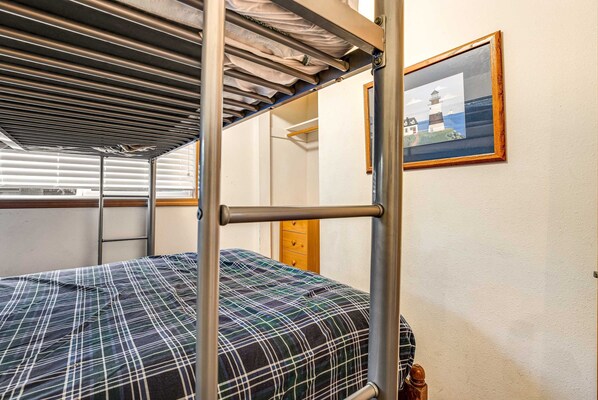 A bunk bed with a plaid bedspread, a wooden wardrobe, and a framed picture of a lighthouse on the wall. - Ocean view home with WiFi, gas fireplaces, private washer&dryer, and foosball (Seaside)