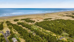 Luchtbeeld van een kustgebied met een strand, bebost gebied en enkele gebouwen.
