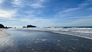 Une plage avec des vagues, un ciel dégagé et des formations rocheuses lointaines.