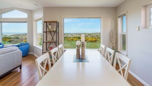 Un espace repas avec vue sur la plage, une table blanche et des chaises.