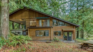 A log cabin with a balcony, large windows, and a deck. - Spacious riverfront lodge with beach access, private hot tub & forest views (Washougal)