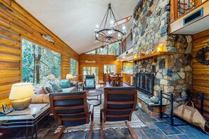 A log cabin interior with a stone fireplace, wooden walls, and a dining area.