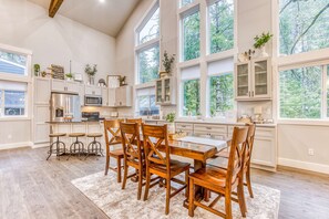 A spacious kitchen with white cabinetry, a large dining table, and bar stools.