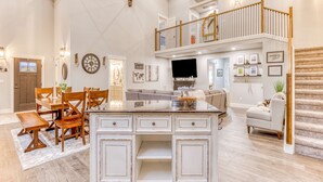 A spacious living area with a dining set, a kitchen, a staircase, and a balcony. - Inviting home with fireplace, sauna, full kitchen, & W&D (Welches)