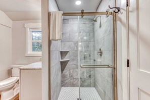 A bathroom with a glass-enclosed shower, a white toilet, and a tiled floor. - Inviting home with fireplace, sauna, full kitchen, & W&D (Welches)