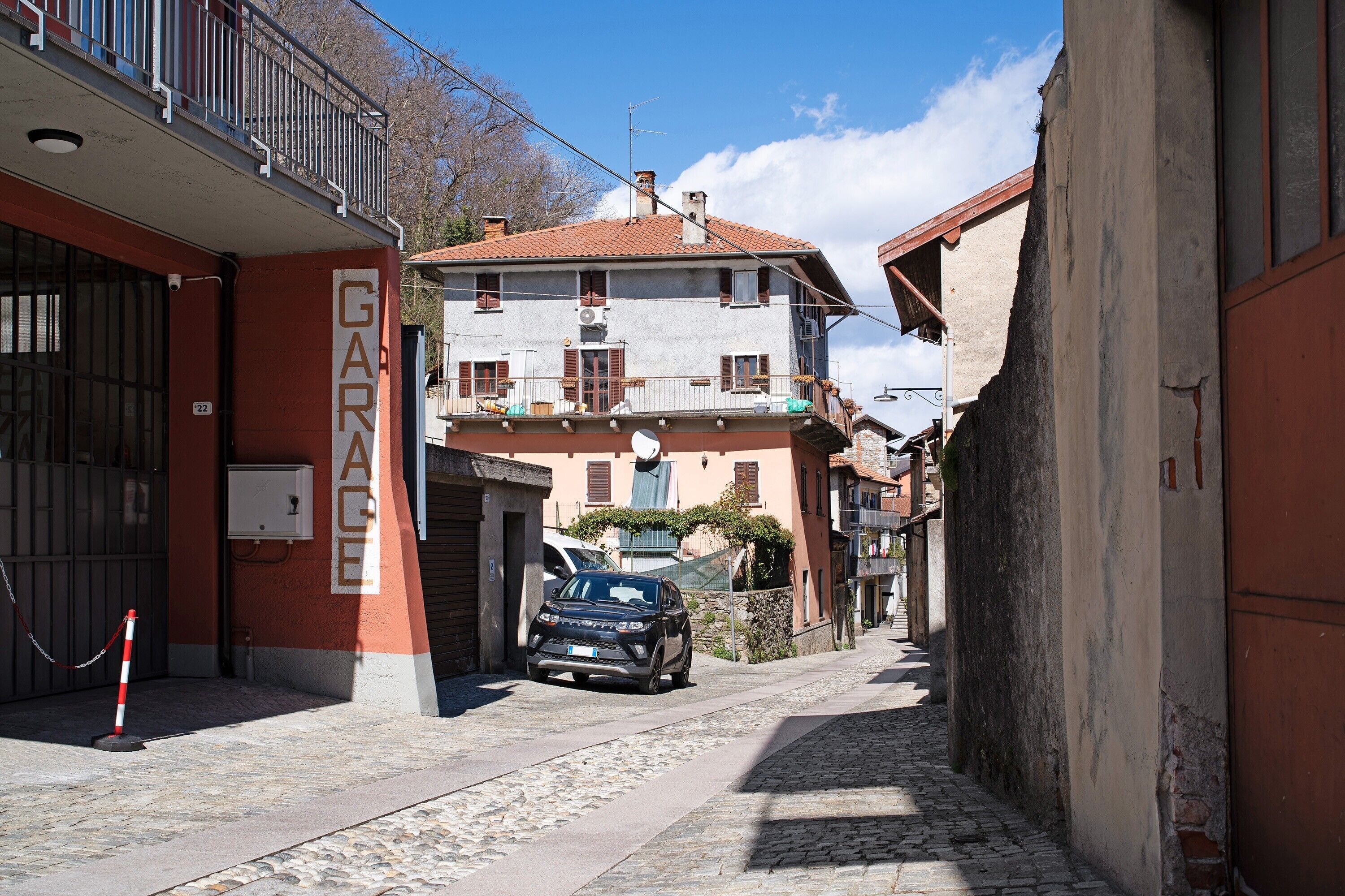 Una calle estrecha con un coche aparcado, edificios con balcones y la entrada a un garaje.