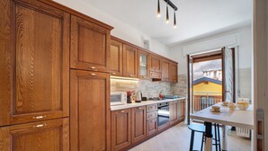 Une cuisine avec des meubles en bois, un plan de travail blanc, une table à manger avec des tabourets et une vue sur un bâtiment à l’extérieur.