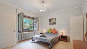 Une chambre à coucher avec un lit, une fenêtre, un radiateur, une table de chevet avec une lampe et une porte.
