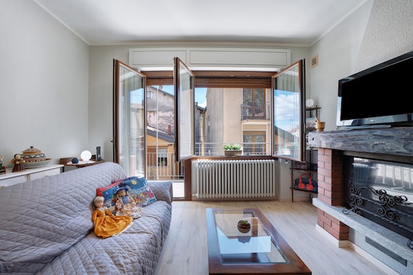 Una sala de estar con sofá, mesa de centro de vidrio, chimenea y televisor.