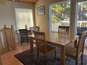 A dining area with a wooden table and chairs, a patterned rug, and large windows with blinds. - 2-story dog-friendly home with beach access, Ping-Pong table, & grill (Manzanita)