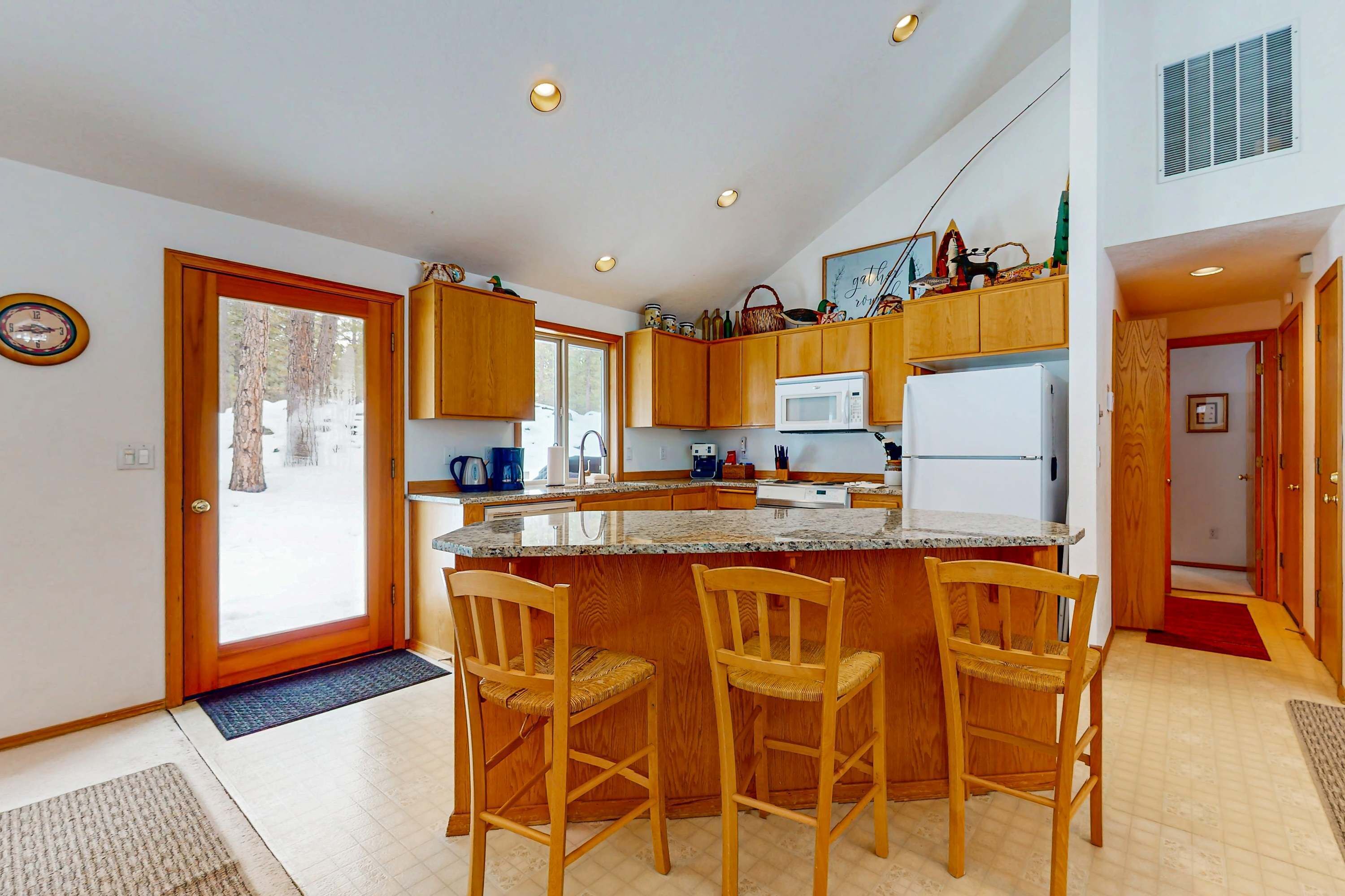 Una cocina con armarios de madera, microondas, refrigerador y una barra con tres sillas.