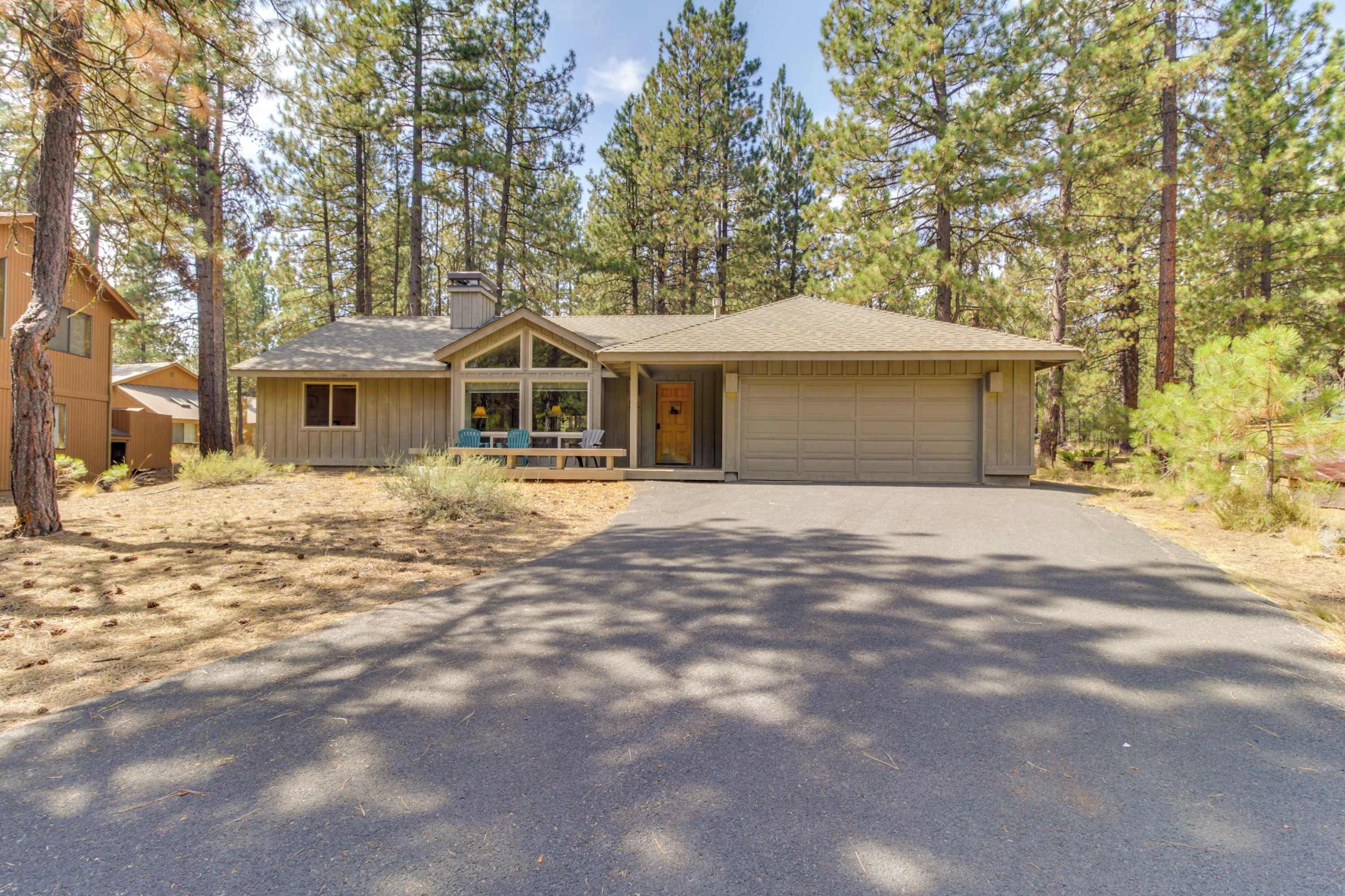 A single-story house with a garage, surrounded by tall pine trees.