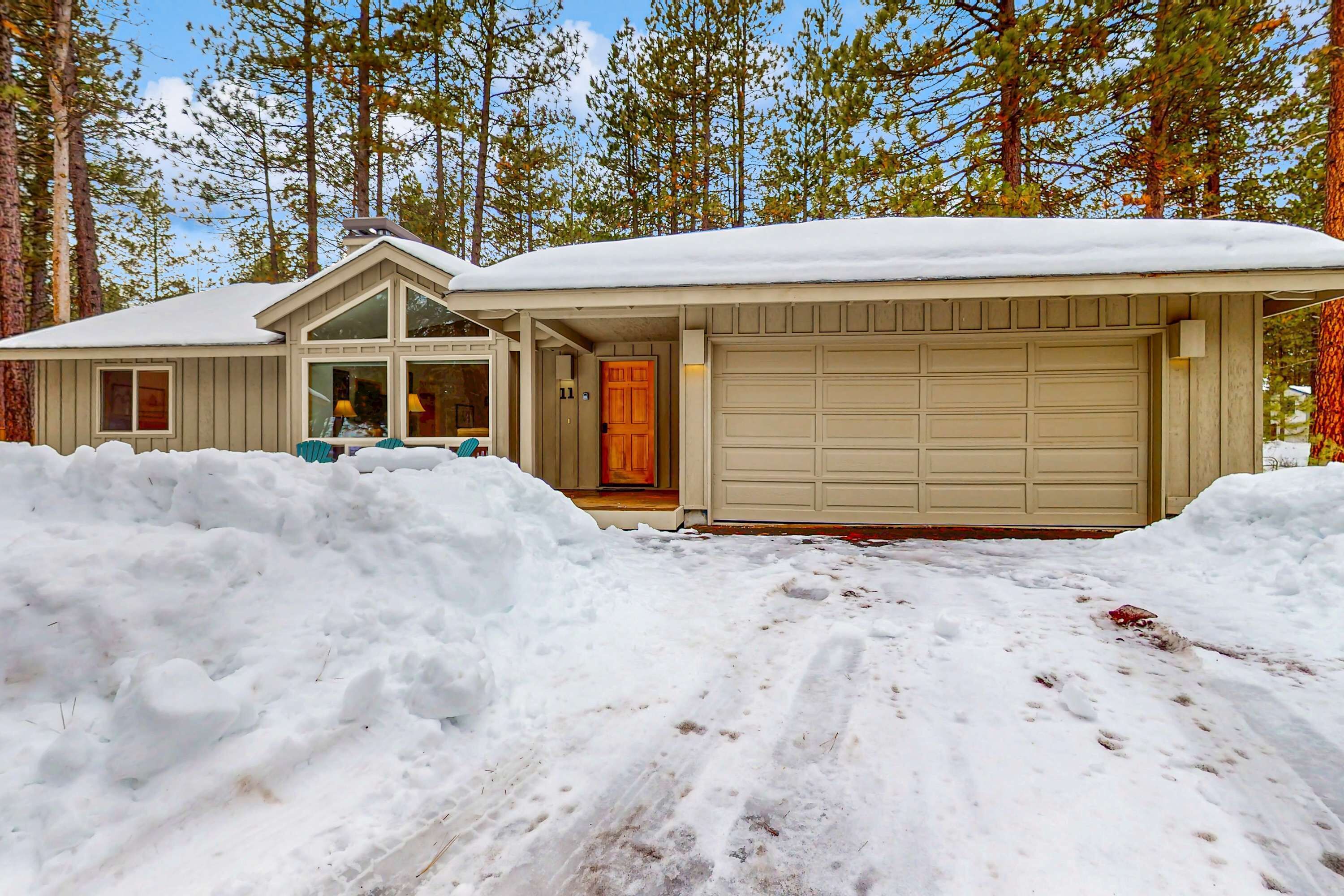 Et hus med garage, omgivet af sne, med en skov i baggrunden.