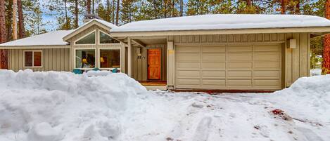 Et hus med garage, omgivet af sne, med en skov i baggrunden.