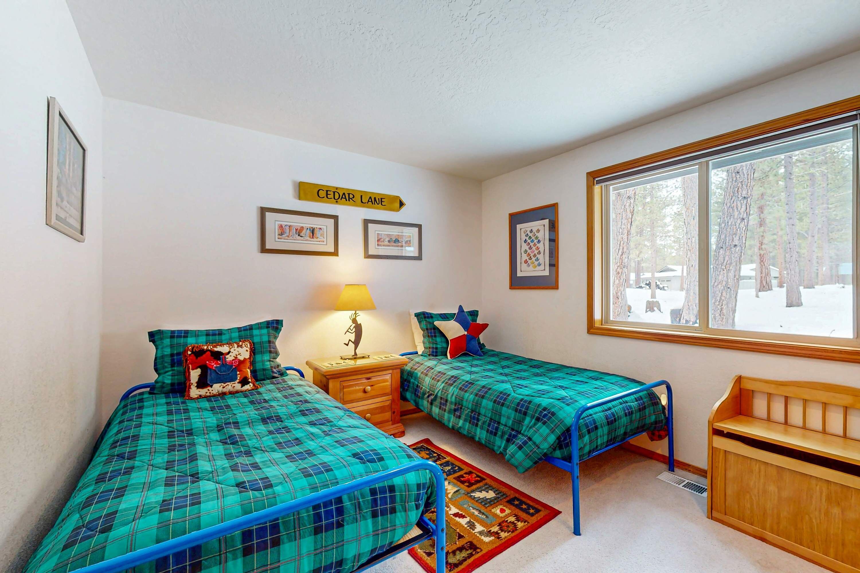 A room with two beds, a nightstand, a lamp, a window with a view of trees, and a sign on the wall.