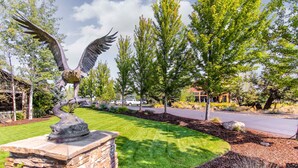 A landscaped area with a bird sculpture, stone wall, and trees. - Spacious getaway near town with private hot tub, pool access, and fast WiFi (Eagle Crest)