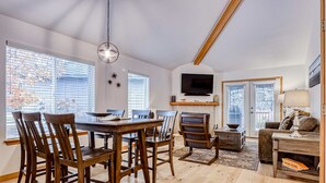 A dining area with a wooden table and chairs, a television mounted above a fireplace, and a sofa in the living area. - Spacious getaway near town with private hot tub, pool access, and fast WiFi (Eagle Crest)