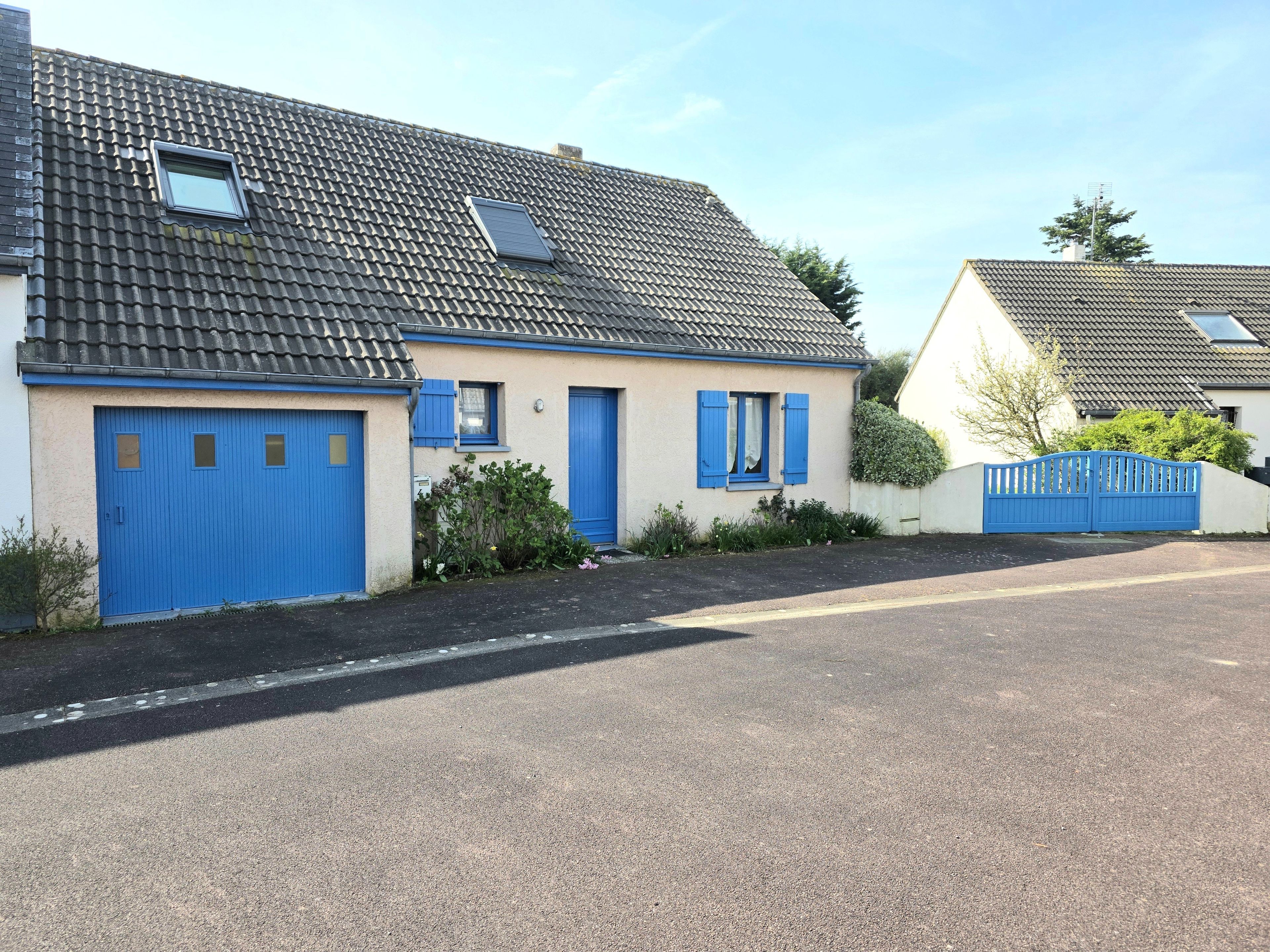 Een woonhuis met pannendak, een blauwe garagepoort en een hekwerk oprit.