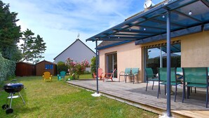 A covered patio with outdoor seating, a barbecue grill, and a wooden deck.