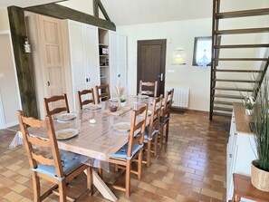 A dining area with a wooden table set for six, surrounded by wooden chairs with blue cushions. - Holiday Home “Les Volets Bleus” with Private Terrace, Garden & Wi-Fi (Pirou)