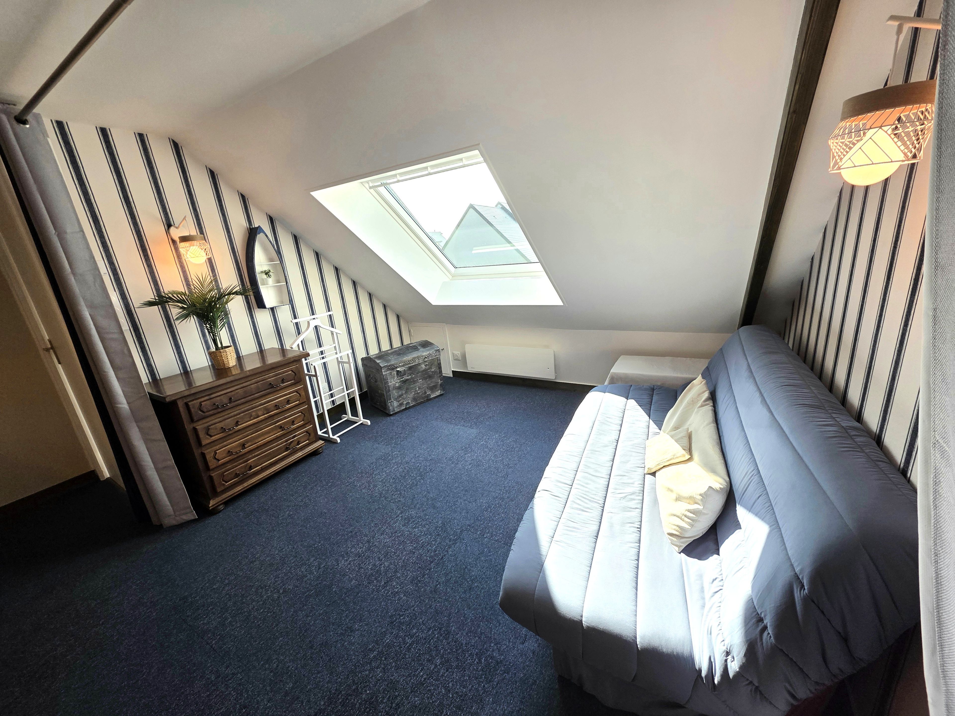 Een slaapkamer met dakraam, een bed, een dressoir en een radiator.