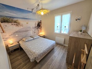 A bedroom with a bed, bedside lamps, a wall mural, a window with curtains, and a wooden cabinet. - Holiday Home “Les Volets Bleus” with Private Terrace, Garden & Wi-Fi (Pirou)