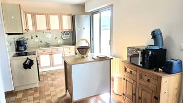 Cocina compacta con cafetera, microondas y tostadora sobre la encimera, armarios de madera y salpicadero de azulejos.