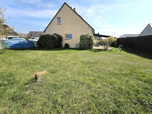 Une maison d’habitation avec un jardin devant, une clôture bleue et un barbecue.