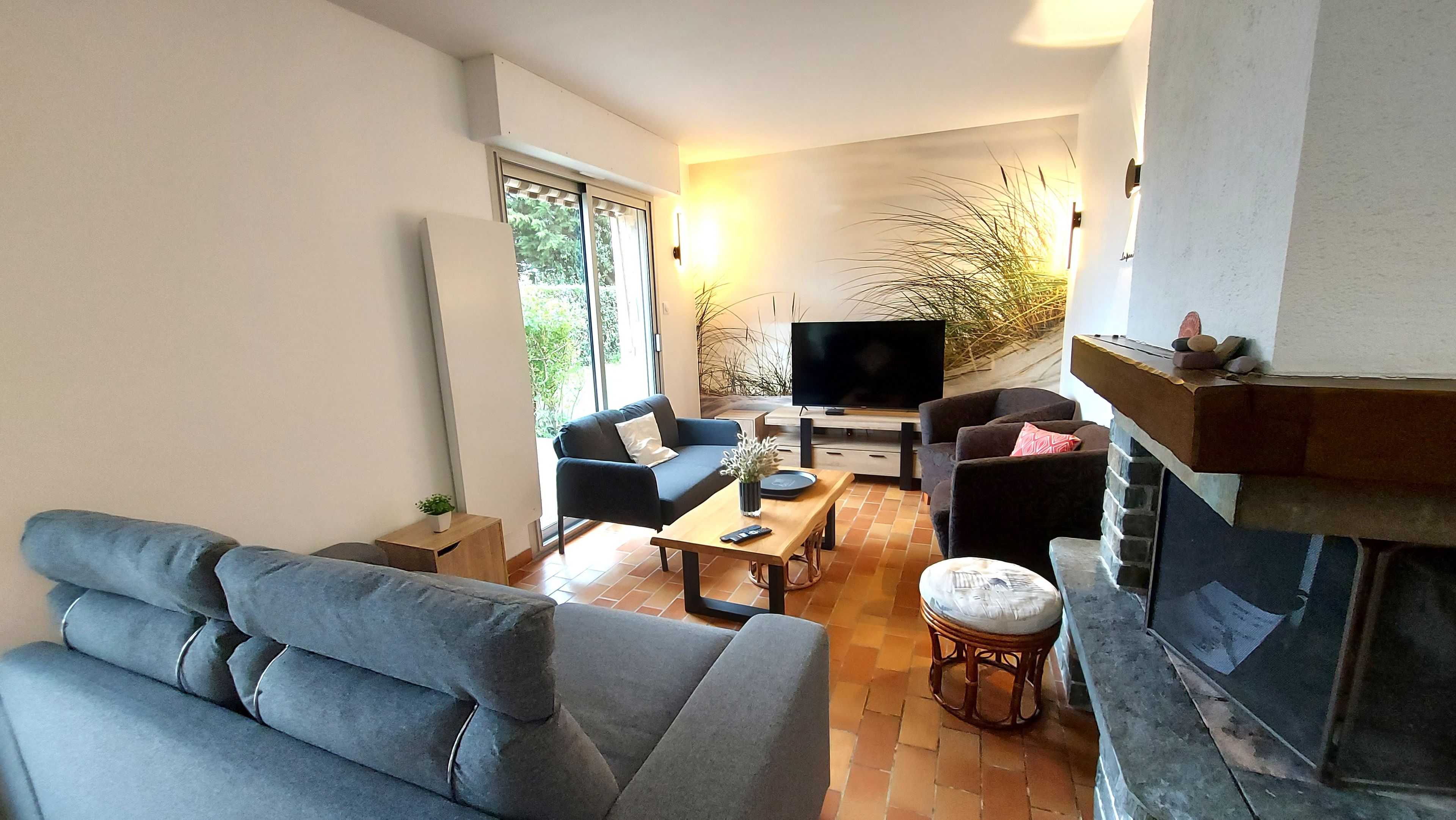 Ein modernes Wohnzimmer mit einer Couch, zwei Sesseln, einem Couchtisch, einem Fernseher und einem Kamin.