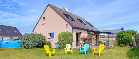A house with a sloped roof, a covered patio, and three outdoor chairs.