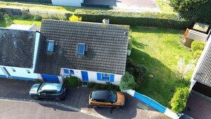Un quartier résidentiel où deux voitures sont garées devant une maison avec un toit en tuiles et des volets bleus.