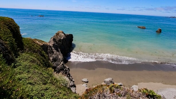Un paisaje costero con aguas azules cristalinas, afloramientos rocosos y una playa arenosa.