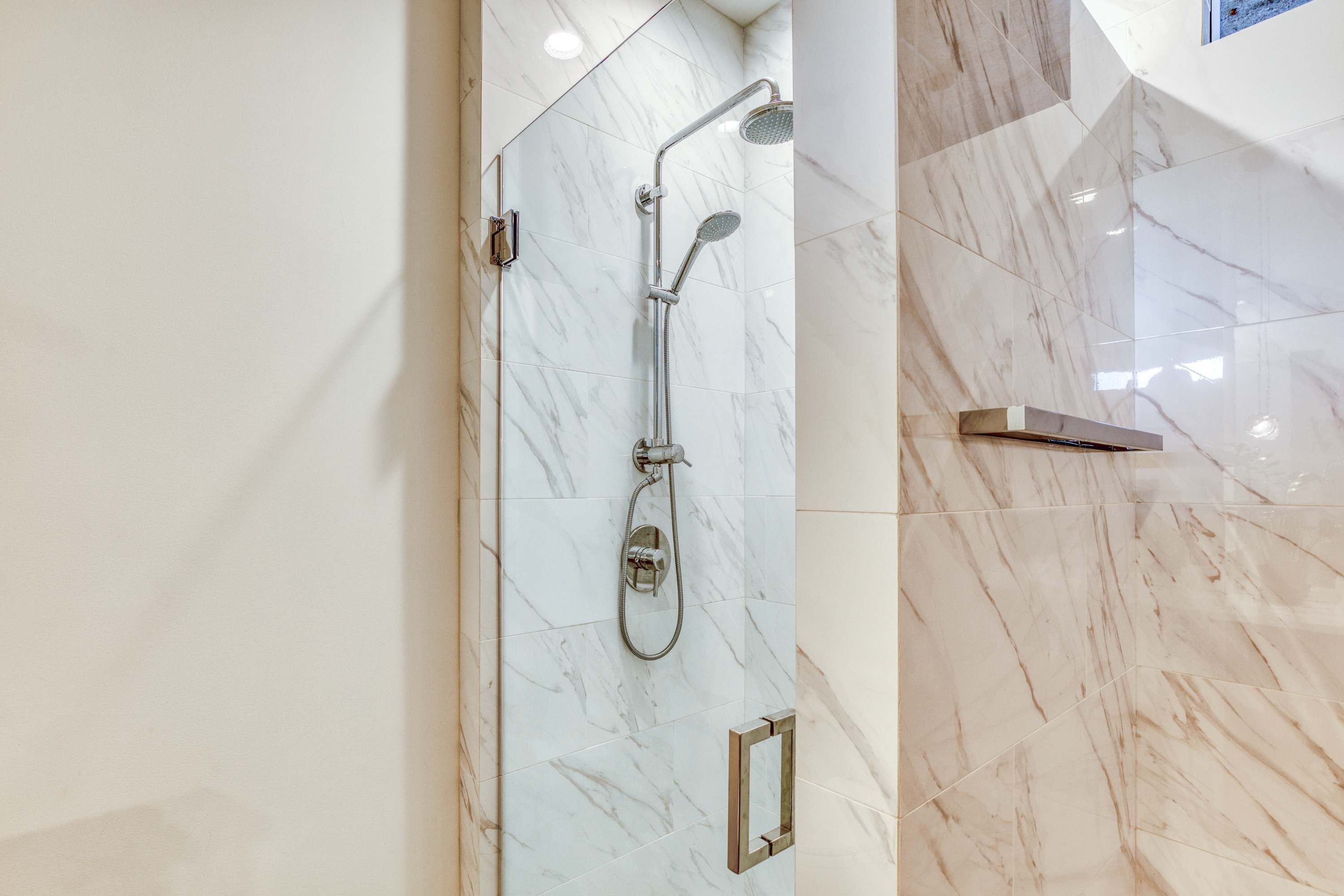 A modern bathroom with a glass-enclosed shower, marble tiles, and a metal towel rack.