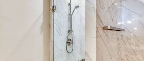 A modern bathroom with a glass-enclosed shower, marble tiles, and a metal towel rack.