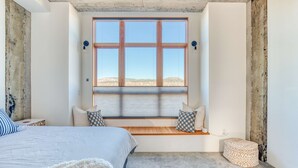 A bedroom with a large window, a bed, a built-in bench, and a small ottoman. - Hood River townhouse close to everything with river-view location & rooftop BBQ (Hood River)