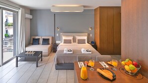 Quarto de hotel moderno com cama, mesas de cabeceira, mesinha de centro e arrumação para café da manhã com frutas e suco.