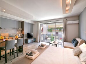 Habitación de hotel moderna con cama, escritorio con televisor, balcón con mesa y sillas, y vistas al exterior.