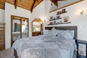 A bedroom with a large bed, wooden headboard, a mirror, and a shelf with pictures. - Big Bear Cabin w/ Hot Tub, Views, Deck & Firepit (Big Bear Lake)