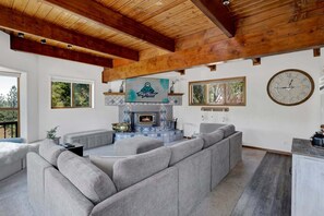 A living room with a fireplace, grey sofas, wooden ceiling beams, and a clock on the wall. - Big Bear Cabin w/ Hot Tub, Views, Deck & Firepit (Big Bear Lake)