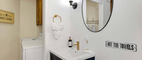 Baño de hotel con lavamanos, espejo, toallero y un cartel que indica 'HOT TUB TOWELS'.