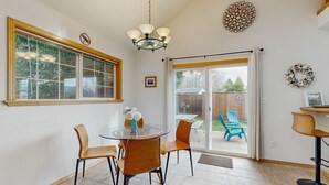 Un coin repas comprenant une table en verre, quatre chaises, un lustre et une porte-fenêtre coulissante donnant sur une terrasse extérieure.