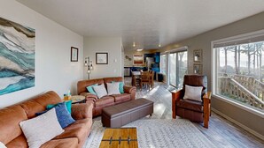 Un salon spacieux avec une grande fenêtre, un canapé en cuir marron, un fauteuil en cuir marron et une table basse en bois.