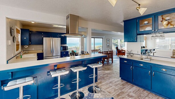 Une cuisine moderne avec des meubles bleus, un réfrigérateur en acier inoxydable et un coin bar avec des tabourets.