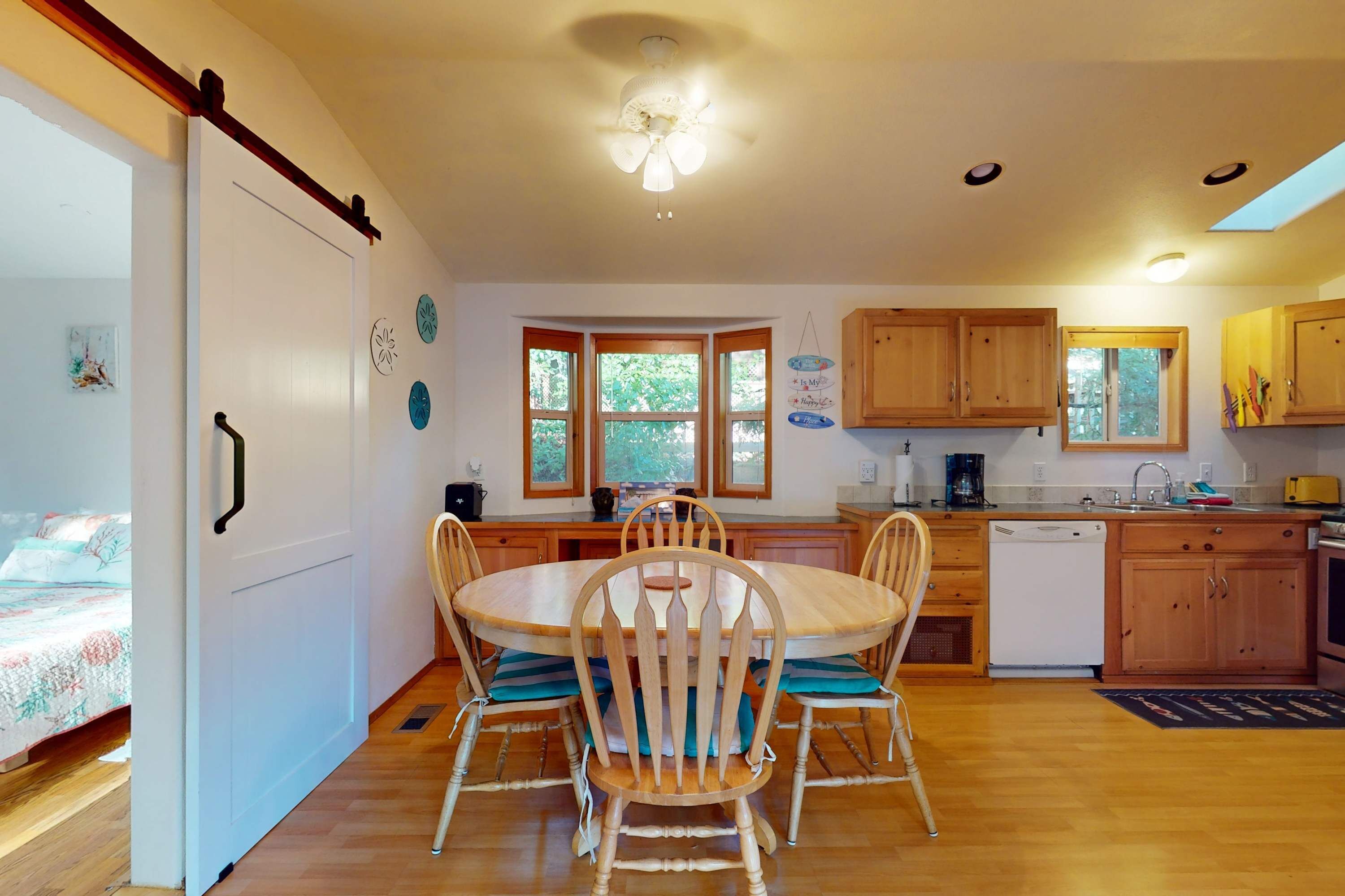 A kitchen with wooden cabinets, a dining table with chairs, a dishwasher, and a window with a view of trees.